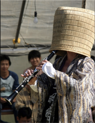 A performer plays a clarinet, wearing a wicker basket over their head. Street vendors and performers depicted in the speculative historical theater, written by Hayashi.