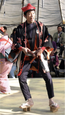 A man mid-stride, performing in block wedge wood thong sandals. Street vendors and performers depicted in the speculative historical theater, written by Hayashi.